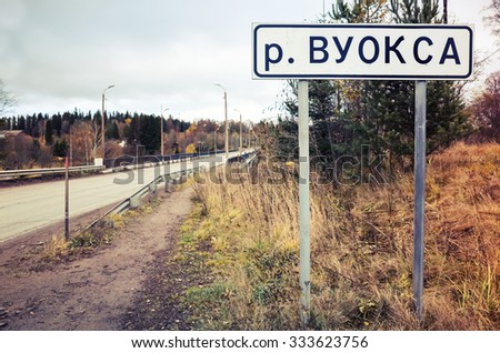 Vuoksa, roadsign with name of Russian and Finnish river and lakes system stands near rural highway. Vintage tonal correction photo filter effect