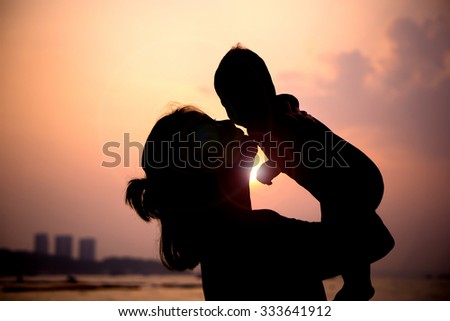 Silhouette of mother  with her toddler against the sunset and lens flare