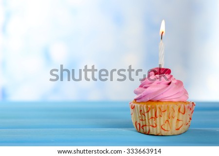 Sweet tasty cupcake with candle on blue wooden table against blurred background