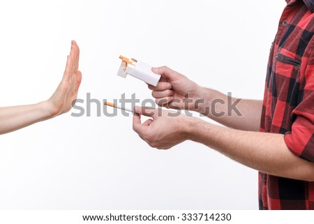 No smoking. Close up of male hands holding cigarettes and proposing it to person. The human arm is gesturing with refusal. Isolated on background