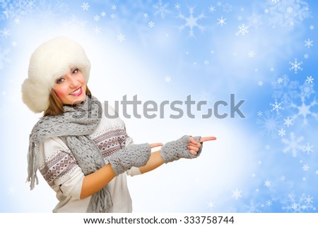 Young girl with fur hat showing pointing gesture on winter background