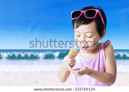 Joyful little girl holding an melting ice cream while enjoying it on the beach