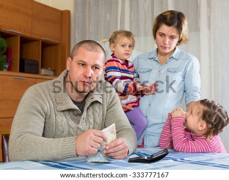Financial problems in family. Unhappy young woman with children against husband at home with money Royalty-Free Stock Photo #333777167