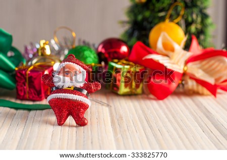 Santa Claus doll against a Christmas tree with gift box on wood background