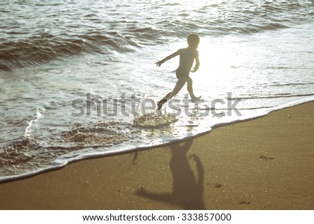 Picture of exciting little boy running on beach beside waves. Vintage image of kid in evening sunlights on seaside background.