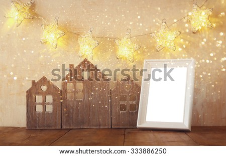 low key image of vintage wooden house decor, blank frame on wooden table and stars garland. retro filtered with glitter overlay. selective focus
