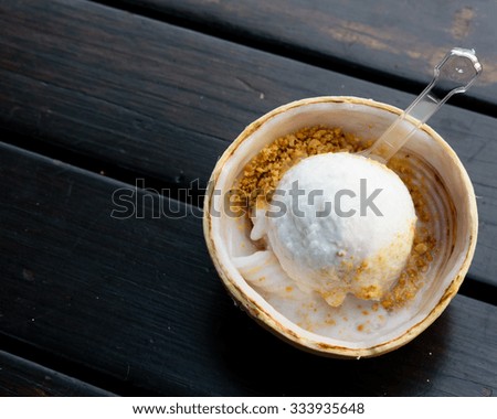 Top view of coconut ice cream strew with ground peanuts scooped into half of coconut shell on a black wooden bench background. Soft dramatic light. Copy space