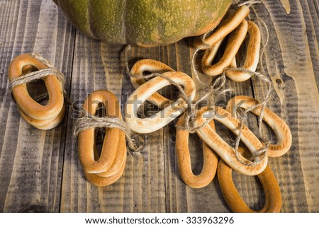 Top distant view closeup rustic autumn still life one big partial fresh orange pumpkin with bunches of hard oval cracknels bind with string on wooden table on timber background, horizontal picture 