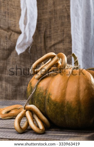 Photo closeup autumn still life one big whole fresh orange pumpkin with bunches of hard oval cracknels bind with string on wooden table on blurred rustic background, vertical picture 
