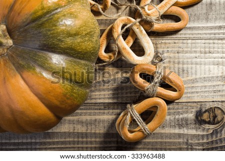 Top distant view closeup rustic autumn still life one big partial fresh orange pumpkin with bunches of hard oval cracknels bind with string on wooden table on timber background, horizontal picture 