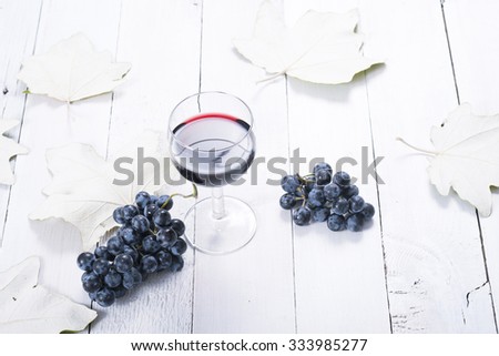 glass of red wine, blue grapes and leaves on white wooden table background