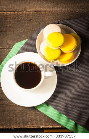 A set of white coffee cup with yellow and green macarons on a rustic wooden background