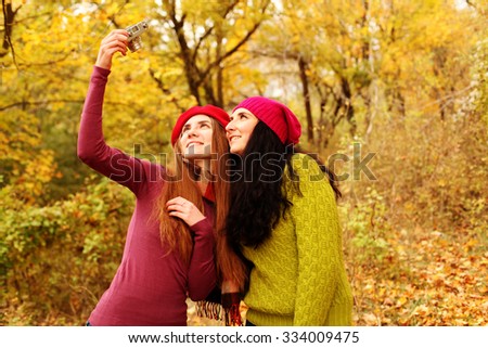Lifestyle fashion portrait of happy stylish girls friends. Two cute girls sisters taking pictures in nature at the autumn park.