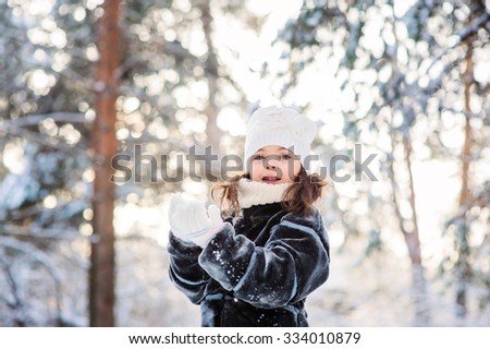 happy child girl playing with snow on the walk in winter forest. Outdoor activity on winter holidays.