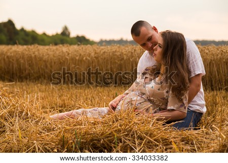 A young man and a pregnant woman sitting in a wheat field of freshly cut wheat. Tenderness and care for the unborn child. Love joyful and sincere feelings. Photo for social magazines websites.