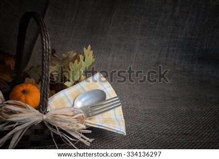 Moody Fall Thanksgiving Still Life with Silver Fork, Spoon, and napkin in a basket with oak leaves.Rustic burlap background and room or space for copy, text, your words. Horizontal and dark vignette.