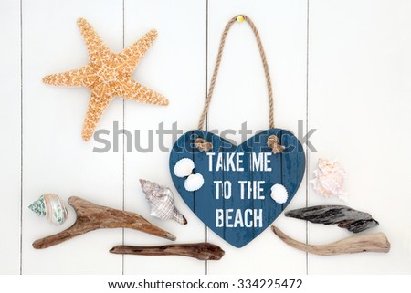 Take me to the beach heart shaped sign with driftwood, starfish and sea shells over white wooden background.