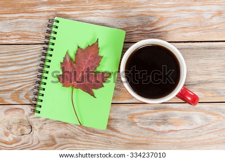 Coffee cup, notebook and autumn leaves on wooden background. Autumn and business background.
