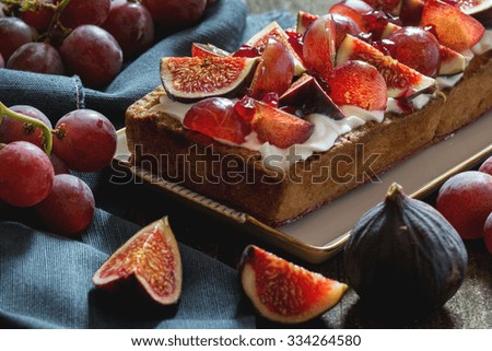 Homemade rectangular Tart with red Grapes, Figs and Whipped cream in white ceramic plate over old wooden table with blue textile rag. Dark rustic style, natural day light.