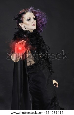 Spooky, black-eyed witch, casting magical red energy from one hand