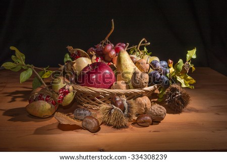 Group of autumnal fruit in a wicker basket, on a wood table and a black curtain as background.