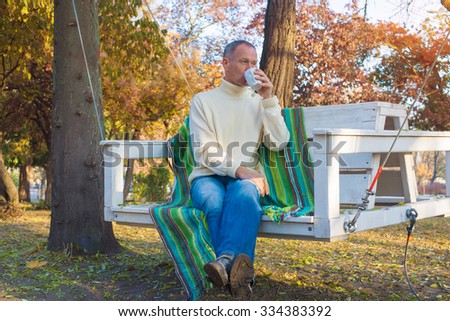 A man relaxing, with cup of coffee  in a autumn park, sitting on swing and thinking about something. Wonderful autumn morning. Soft light.