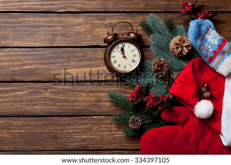 Alarm clock and pine branch with Santa Claus clothes on wooden background