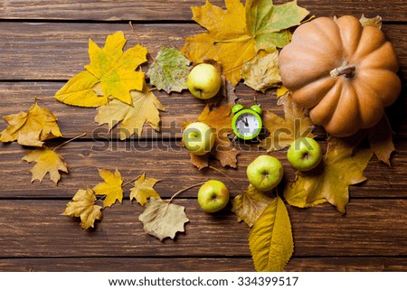 Apples and alarm clock with pumpkin and leafs on wooden table.