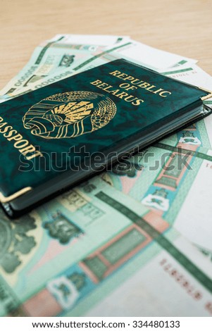 Passport of Republic of Belarus in green cover with Belarusian rubles lying on wooden table.