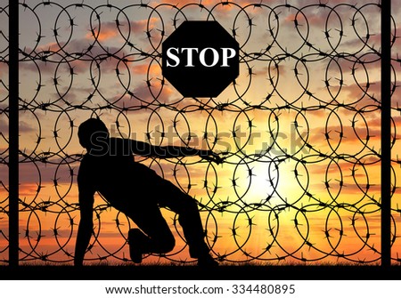 Concept of the refugees. Silhouette of illegally crossing the border and refugee stop sign on a fence with barbed wire