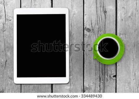 White tablet with a green coffee cup on old wooden table. Blank screen with space for copy. Concept the coffee break with the use of the tablet.