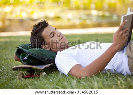 Student with skateboard and backpack reading in the grass
