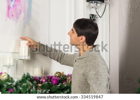 Portrait of young man decorating mantel with candles, christmas garland, baubles, ribbons, pine cones and orchid
