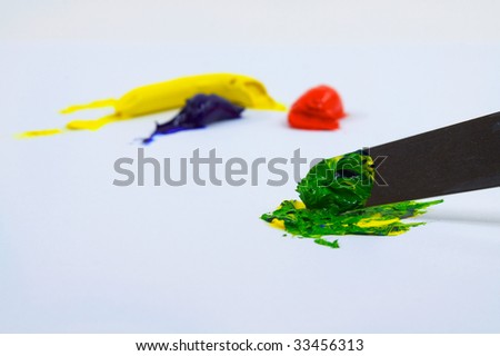 Yellow, blue, and red paint blobs being mixed by an artiists pallete knife