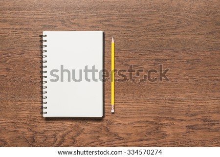 yellow pencil with blank note book on wooden background, top view