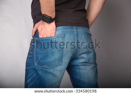 Backside of a young fashion man in jeans with phone in pocket  on gray background