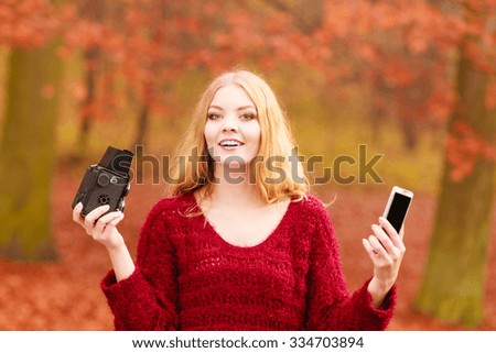 Pretty smiling woman in fall forest park taking selfie self photo with old vintage camera and smartphone. Happy gorgeous young girl photographer. Autumn winter photography.
