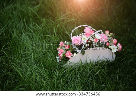 Closeup view of one beautiful decorative holiday flowers of pink white rose and other in bag standing on fresh bright green grass on natural background, horizontal picture