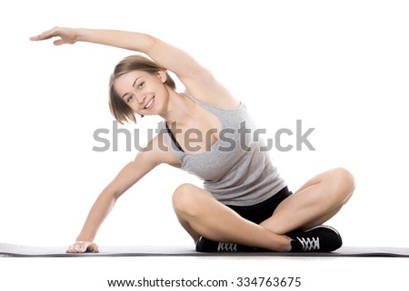 Portrait of young cheerful slim sporty beautiful woman working out on mat, warming up, sitting with crossed legs doing exercises for waist, isolated studio image on white background