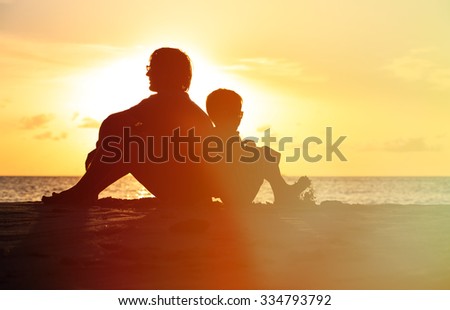 father and son looking at sunset on tropical beach