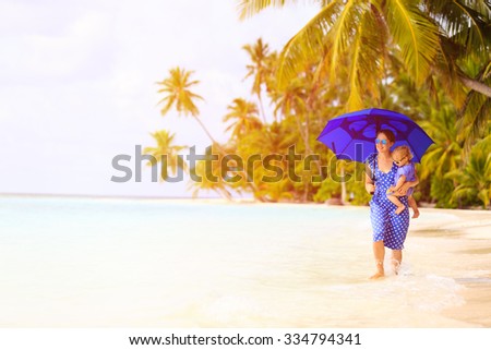 mother and little daughter walk on beach with umbrella to hide from sun