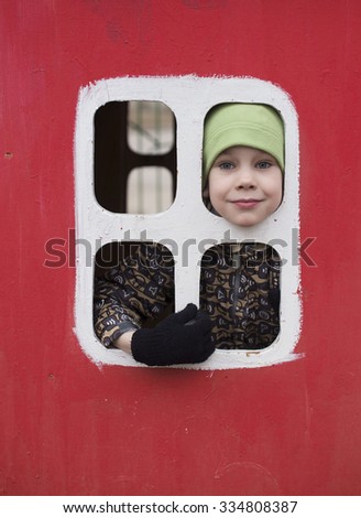 boy in toy wooden house. child in warm clothes looking out the window in a toy house on the Playground