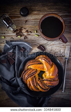 Sweet pastry with poppy seeds and cup of black coffee on vintage wooden table, top view. Warm tones. Breakfast in cafe. Vertical composition