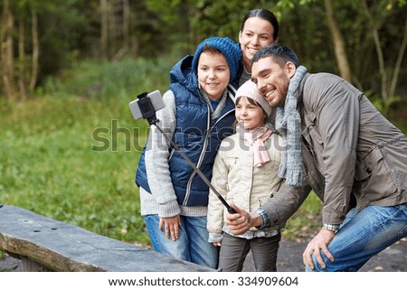 camping, tourism, hike, technology and people concept - happy family taking picture with smartphone on selfie stick at camp