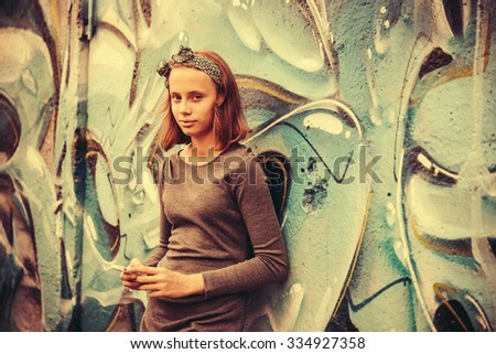 A teenage girl with smartphone leaning against the wall with graffiti. Toned image