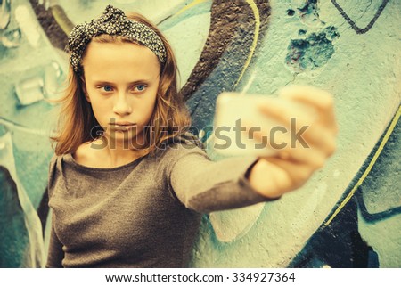 A teenage girl takes selfie with graffiti in the background. Toned image