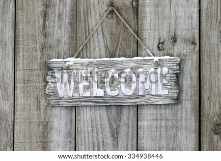 Rustic wooden welcome sign with snow hanging on antique weathered wood background; winter Olympics welcome sign