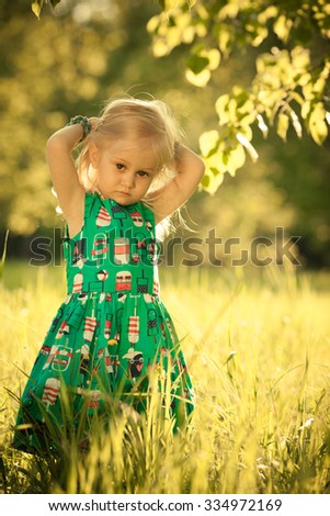 Adorable little sad girl staying under the tree. Summer green grass