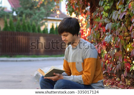 Educational concept. Young handsome man reading old book. Autumn background.