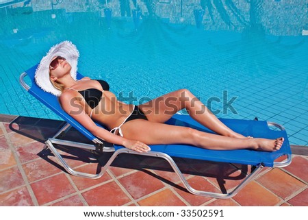 Young blond white woman lying on blue sunbed at swimming pool.